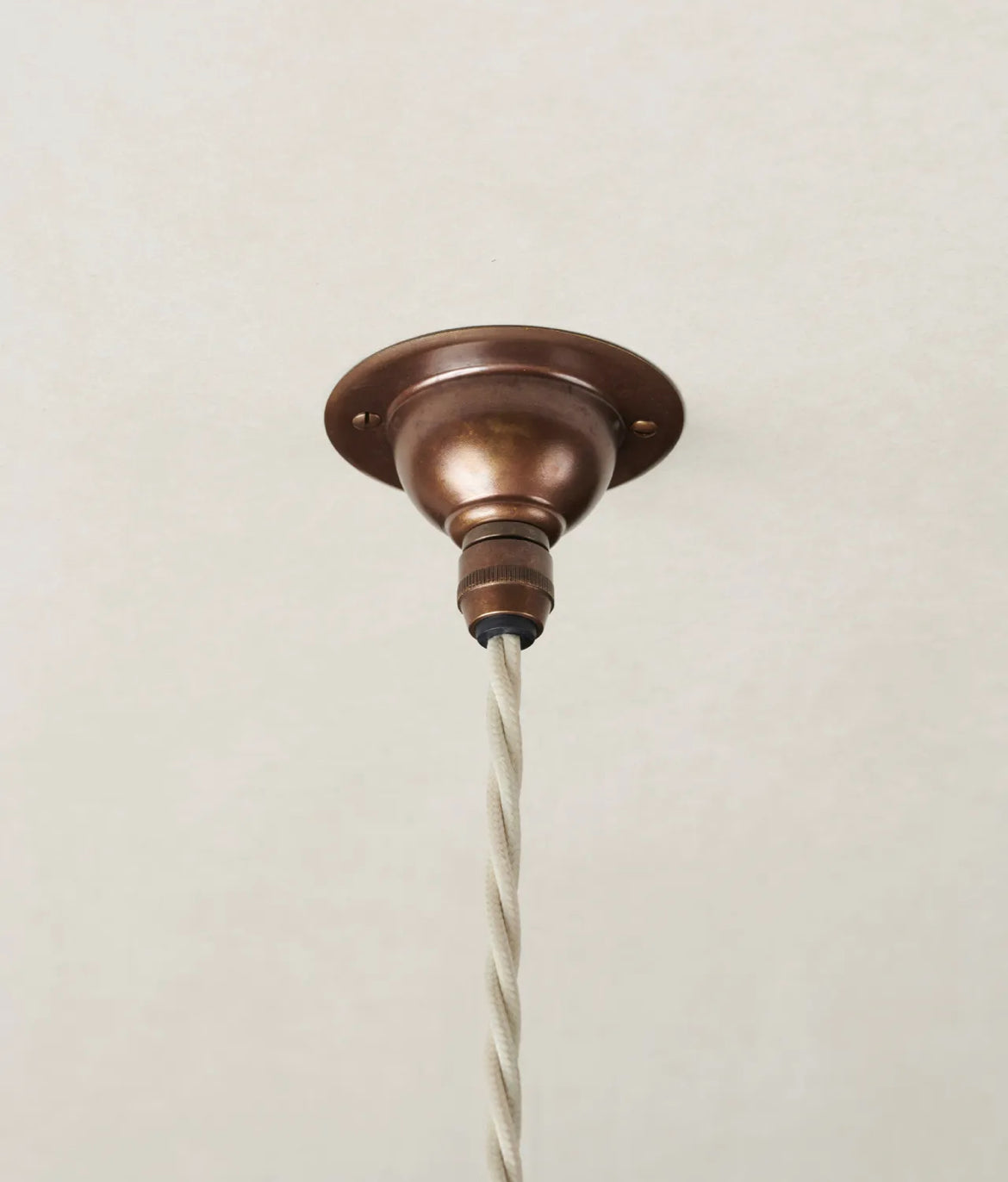 Bronze ceiling light fixture with white cord on a beige background