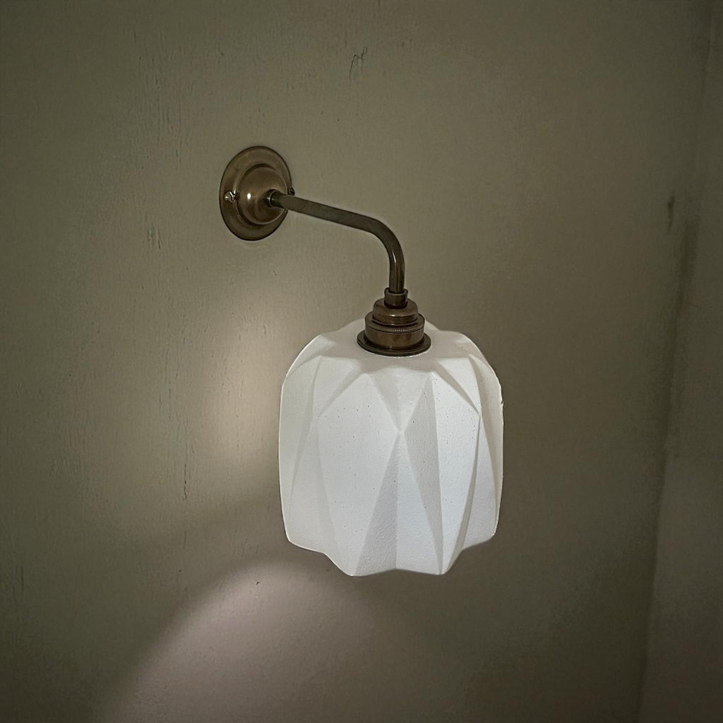 handmade wall lighting fixture with geometric white glass shade on a plain wall.