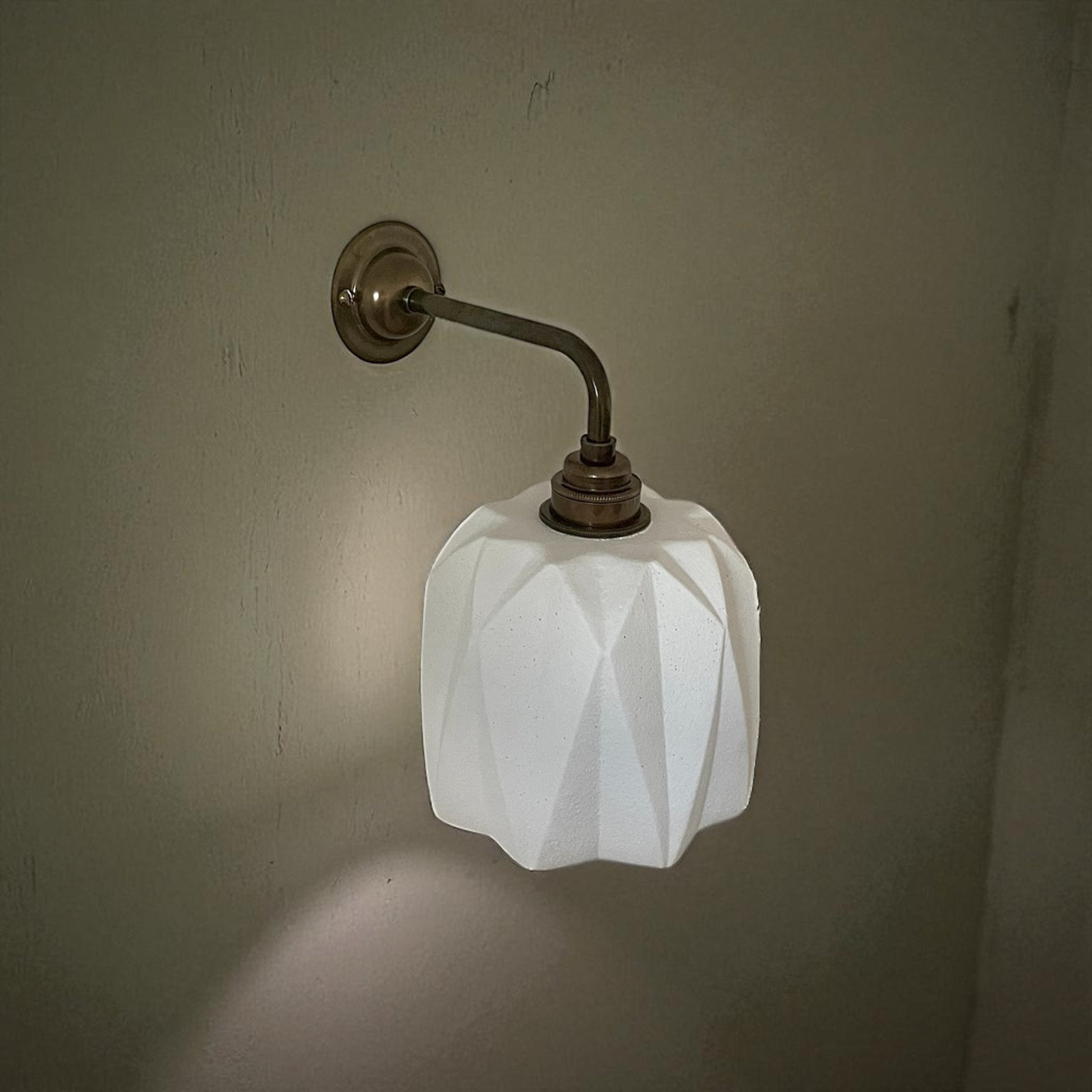 handmade wall lighting fixture with geometric white glass shade on a plain wall.