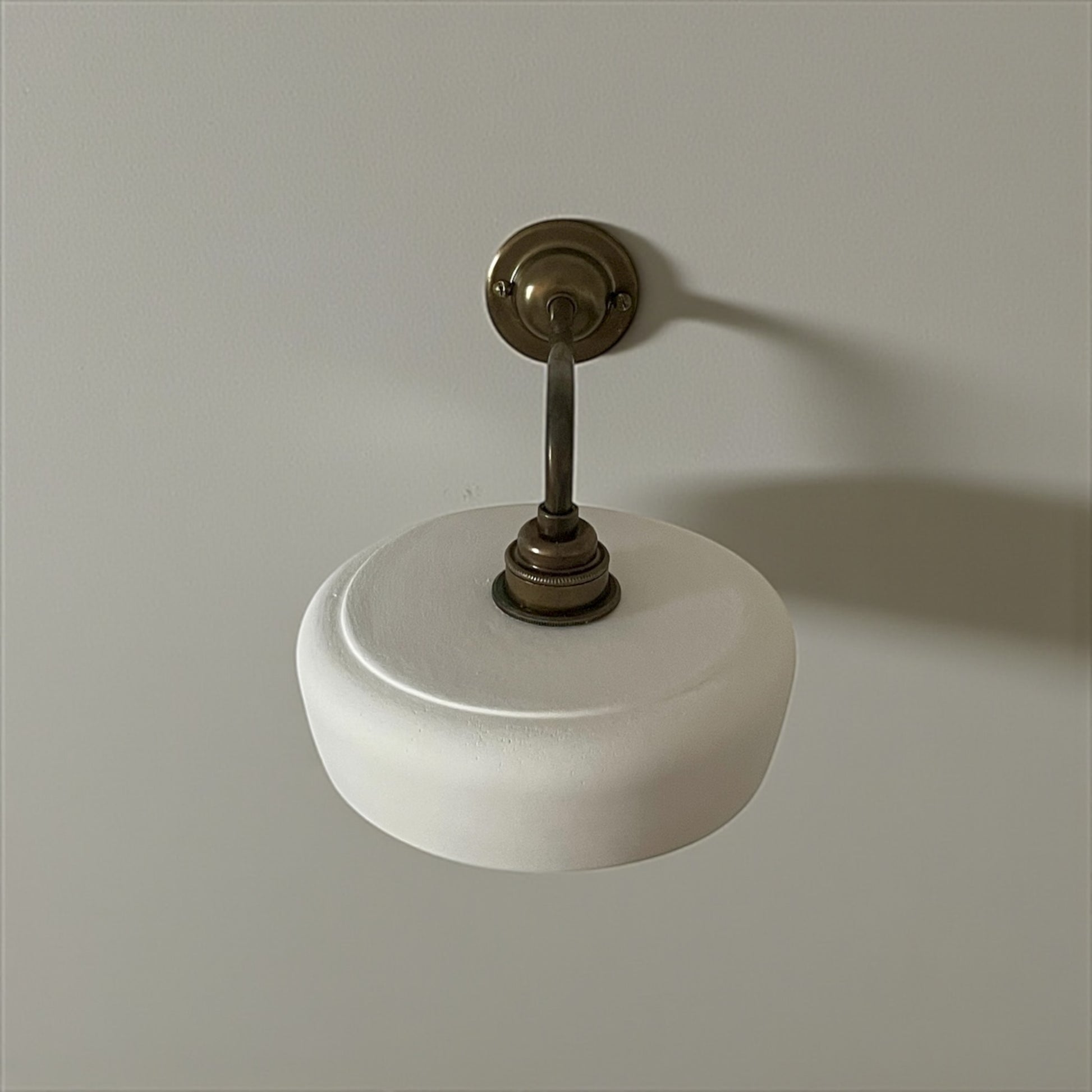 Wall light with white shade and brass fitting on a plain wall.