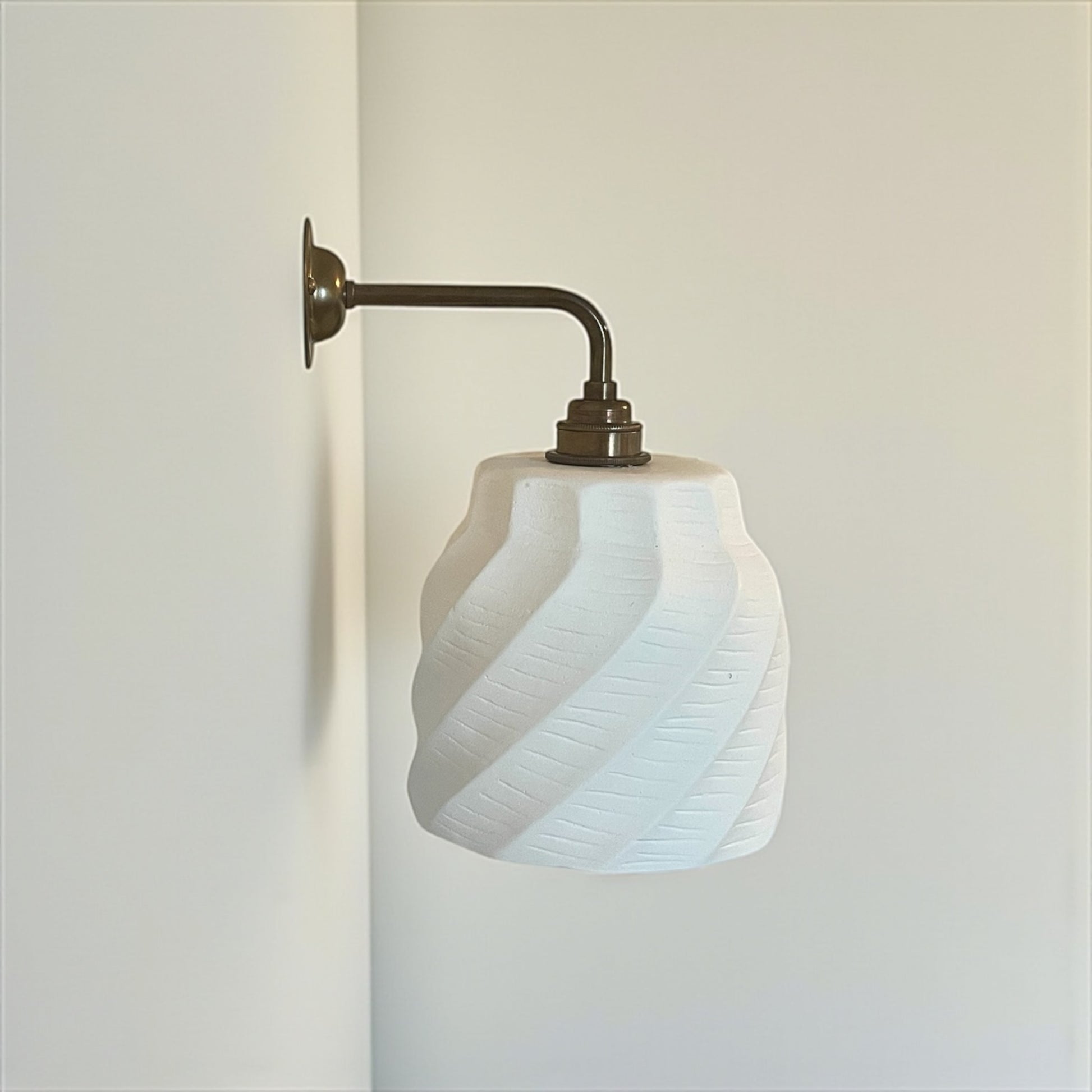 handmade Wall-mounted lamp with a white glass shade and brass fixture on a plain wall.