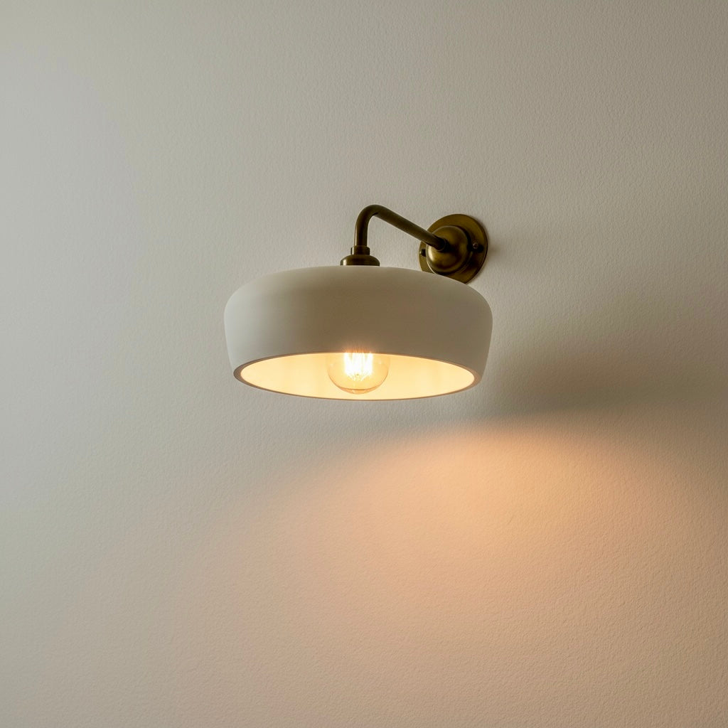 Handmade minimalist wall light with a white shade and brass arm on a plain wall.