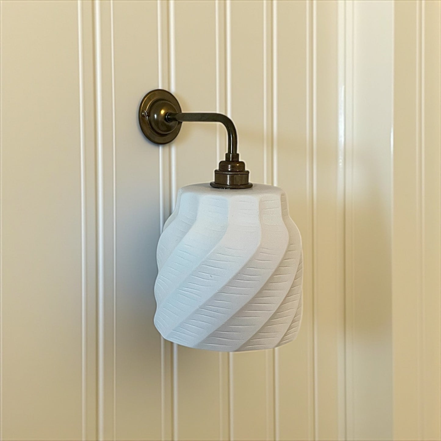 minimalist wall sconce with white glass shade and brass fixture on a beige paneled wall.
