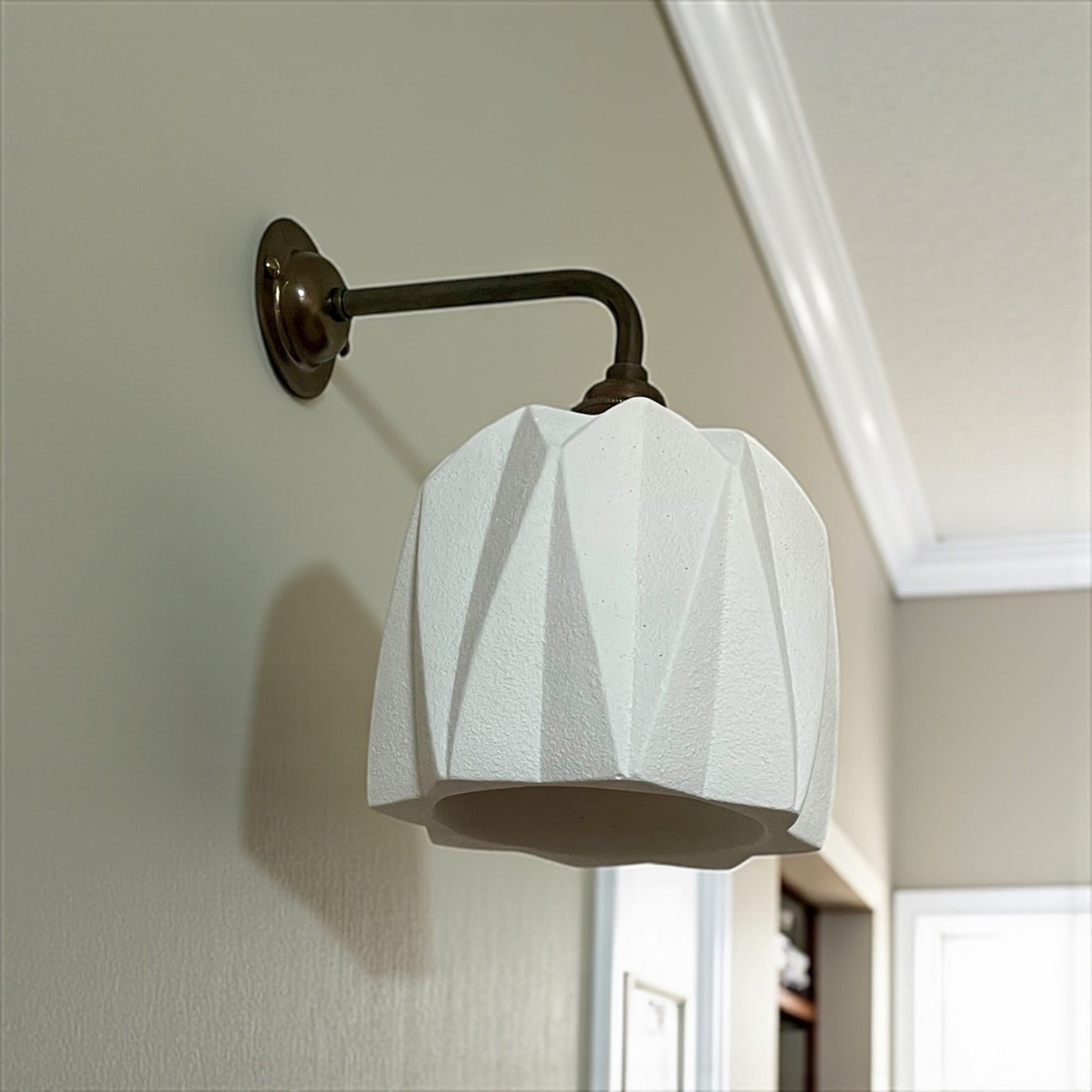 handcrafted wall lighting fixture with white glass shade and brass arm on a neutral wall.