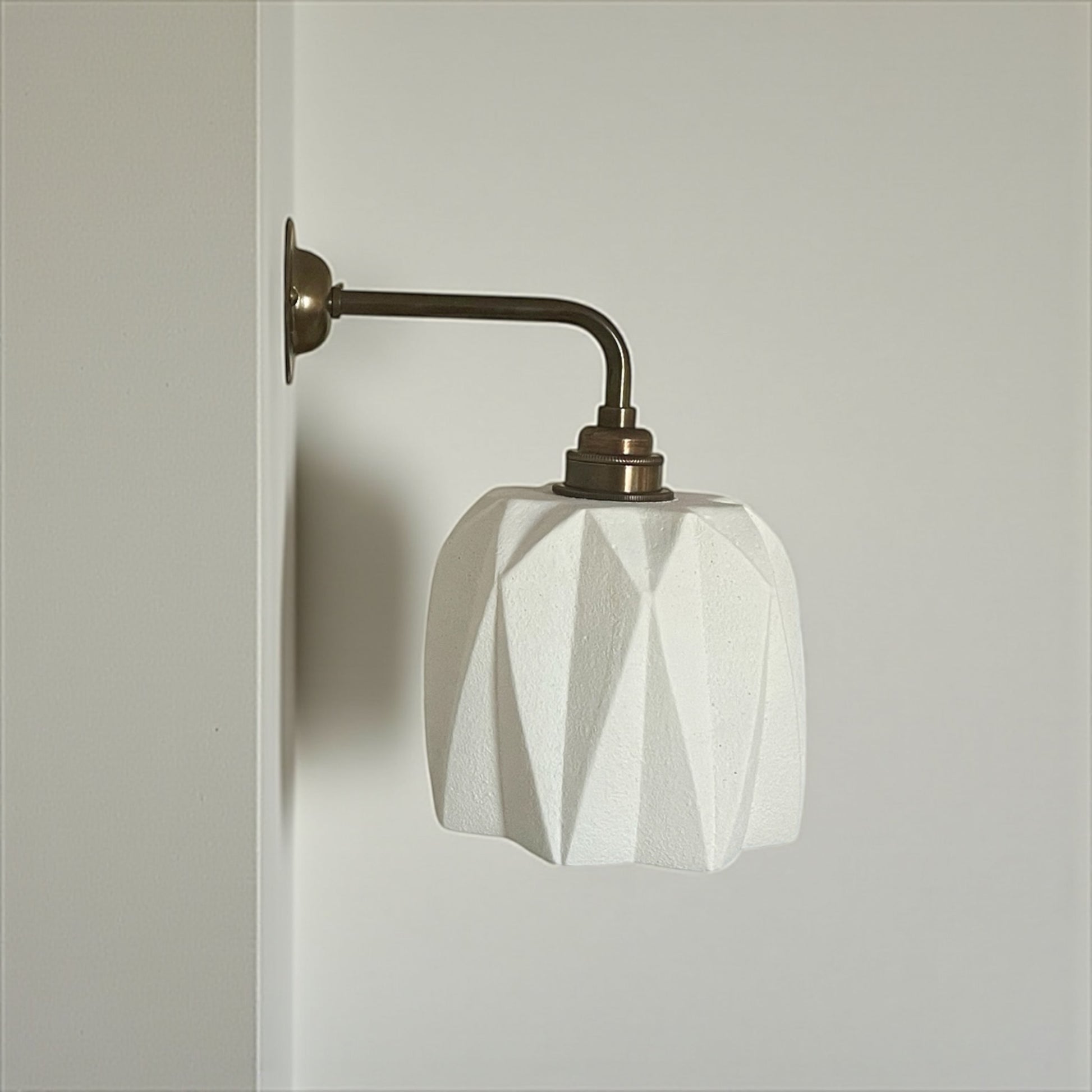 handmade wall sconce with geometric white shade and bronze arm on a neutral background
