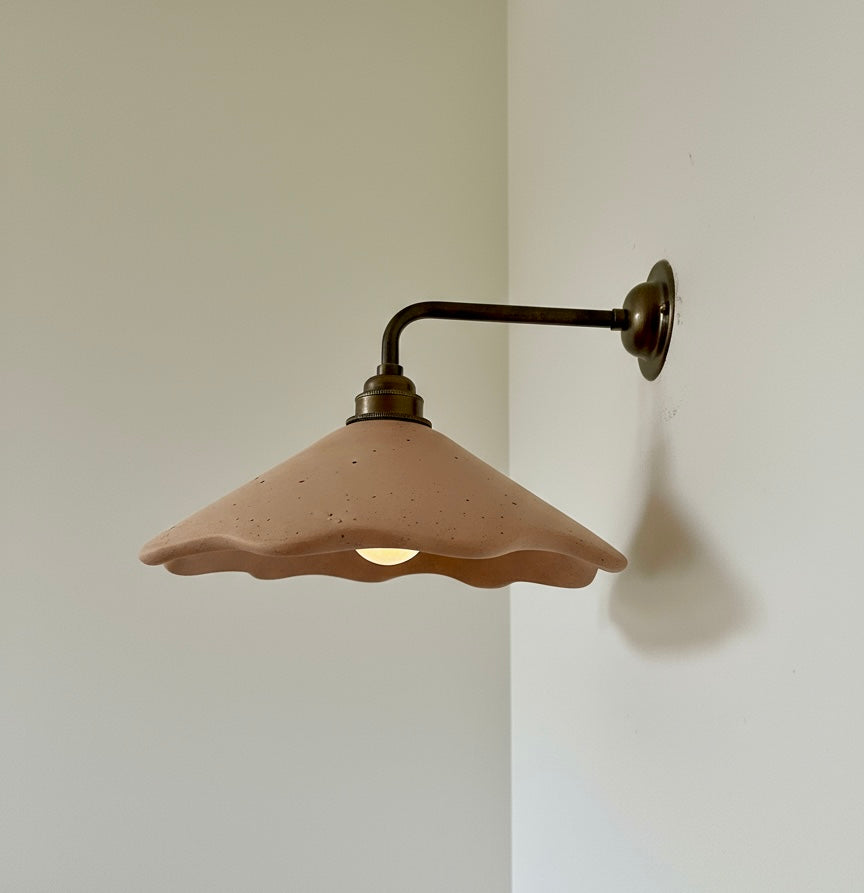 Wall-mounted light fixture with a plaster terracotta shade on a plain wall.