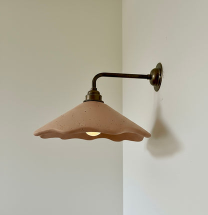 Wall-mounted light fixture with a plaster terracotta shade on a plain wall.