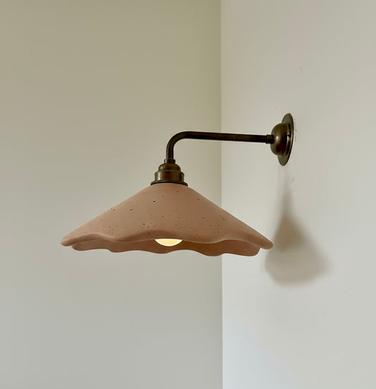 Wall-mounted light fixture with a plaster terracotta shade on a plain wall.
