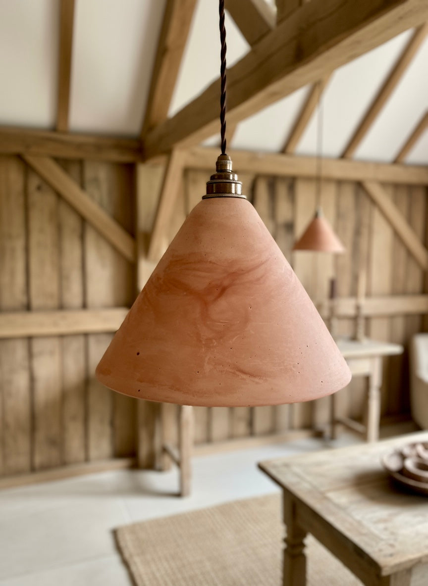 Terracotta pendant light hanging in a rustic wooden room with a table and chairs.