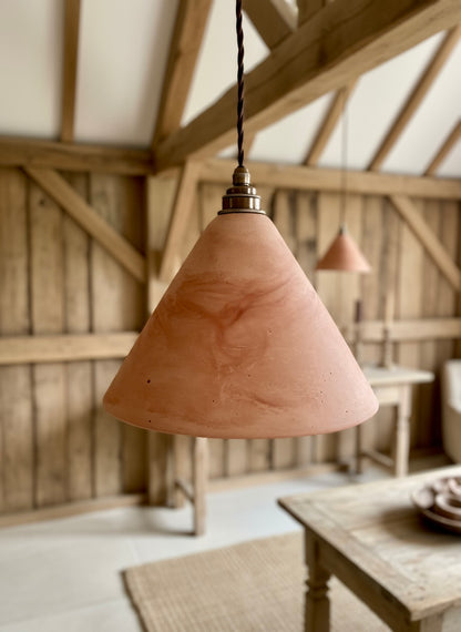 Terracotta pendant light hanging in a rustic wooden room with a table and chairs.