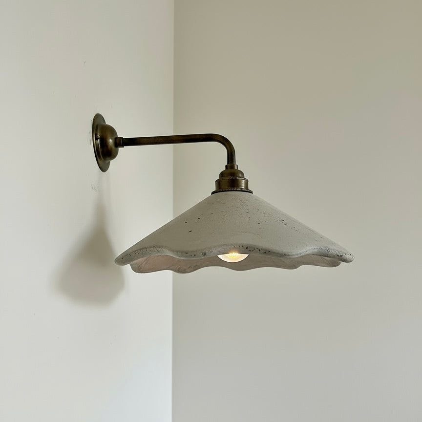 Wall-mounted light fixture with a white shade and brass arm on a plain wall.