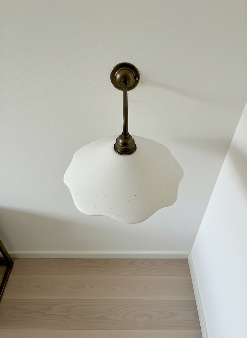 Wall lamp fixture with white glass shade and brass fixture on a plain wall.