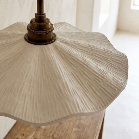 A close-up of a textured, scalloped cream-colored glass or resin pendant lamp shade with a bronze-finished metal fixture, resting on a rustic wooden surface.