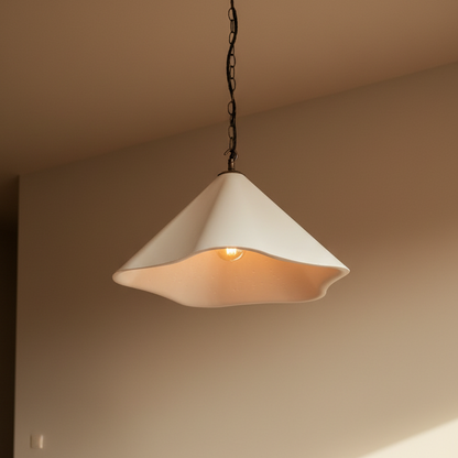 A modern pendant light with a wavy, scalloped white shade hanging over a wooden cabinet in a warm, minimalist room.