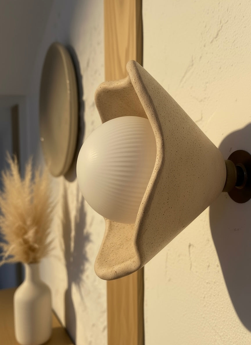 Close-up of a sculptural beige wall light bulb on a brass fixture against a neutral wall.
