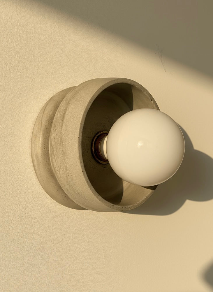 Concrete grey plaster wall sconce with a white bulb on a beige background