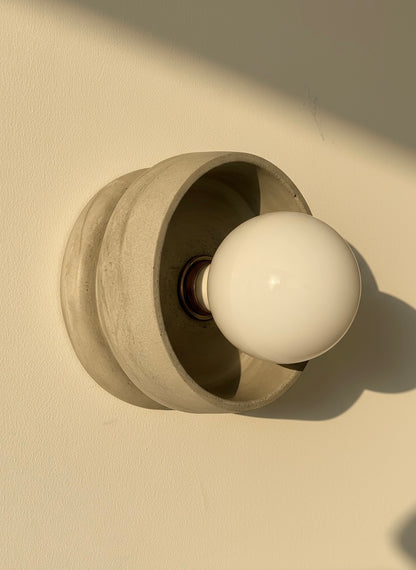 Concrete grey plaster wall sconce with a white bulb on a beige background