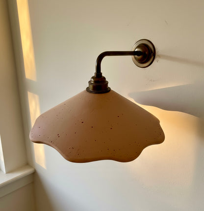 Wall-mounted lamp with a terracotta lampshade on a white wall.