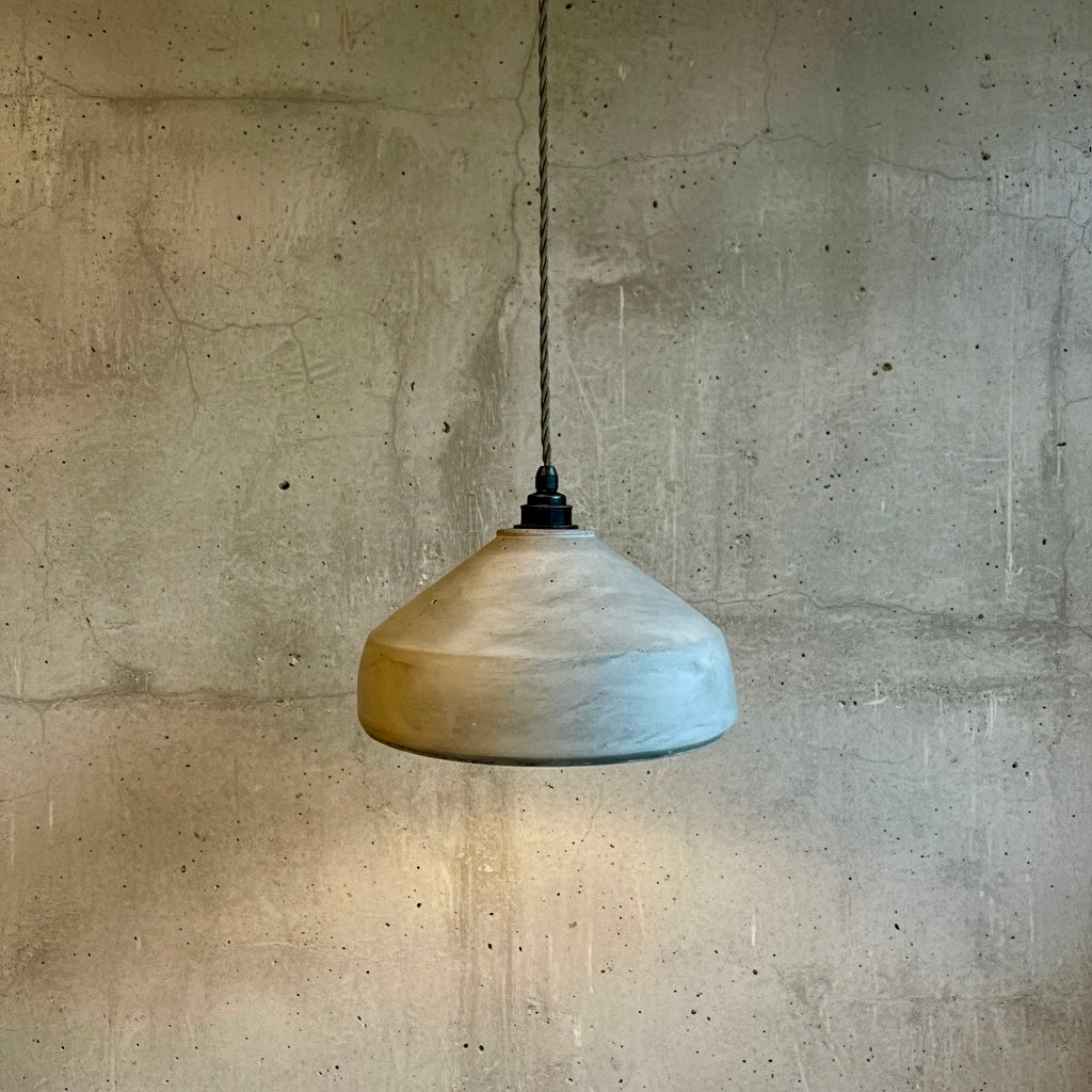 Handmade plaster pendant light hanging against a textured concrete wall