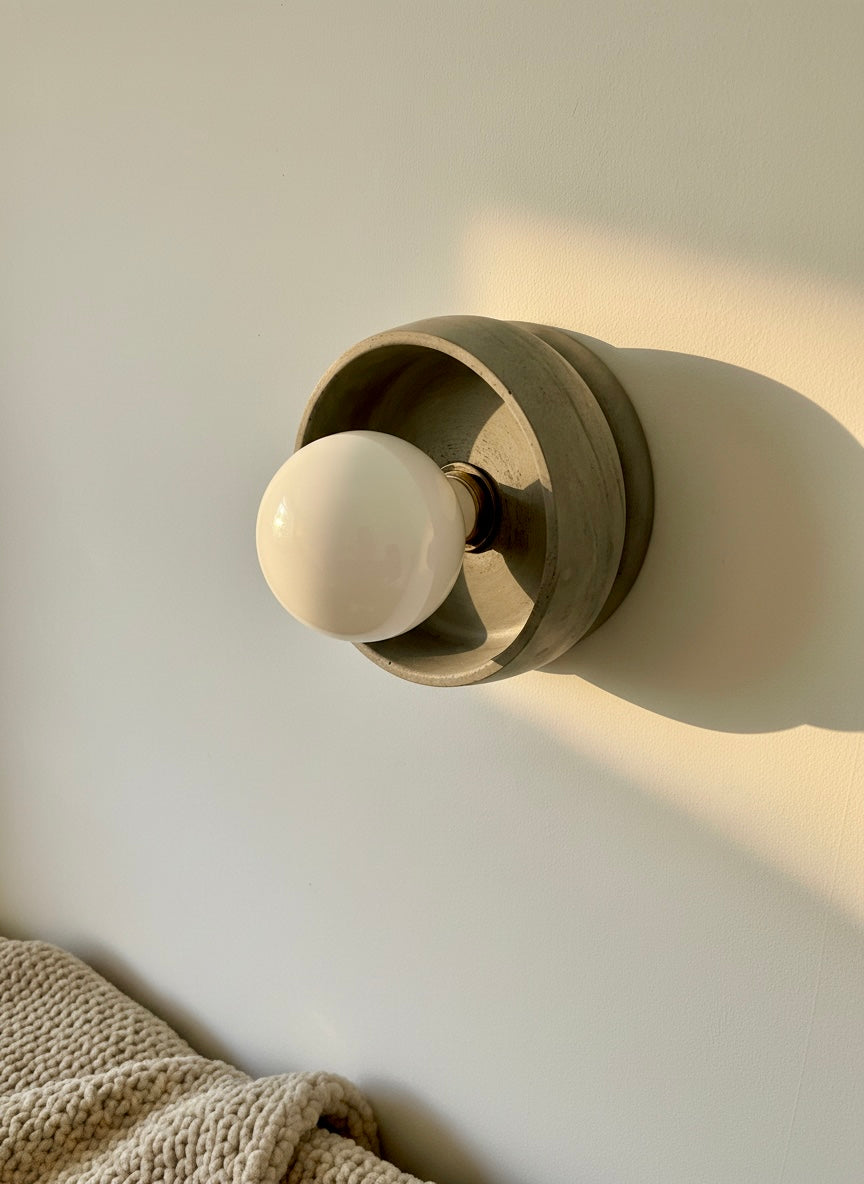 Flush mount grey wall light fixture with a white bulb on a neutral wall.