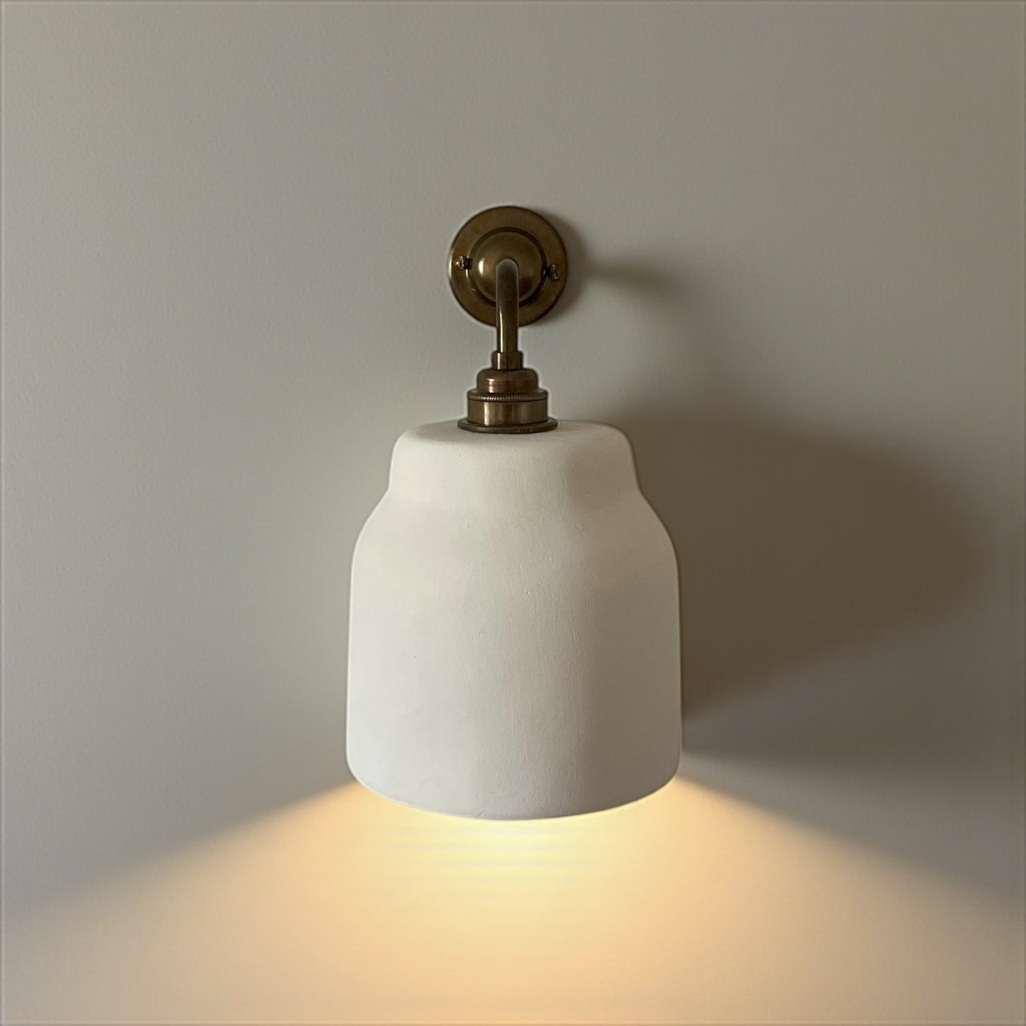 Wall light fixture with white ceramic shade and brass fitting on a neutral wall.