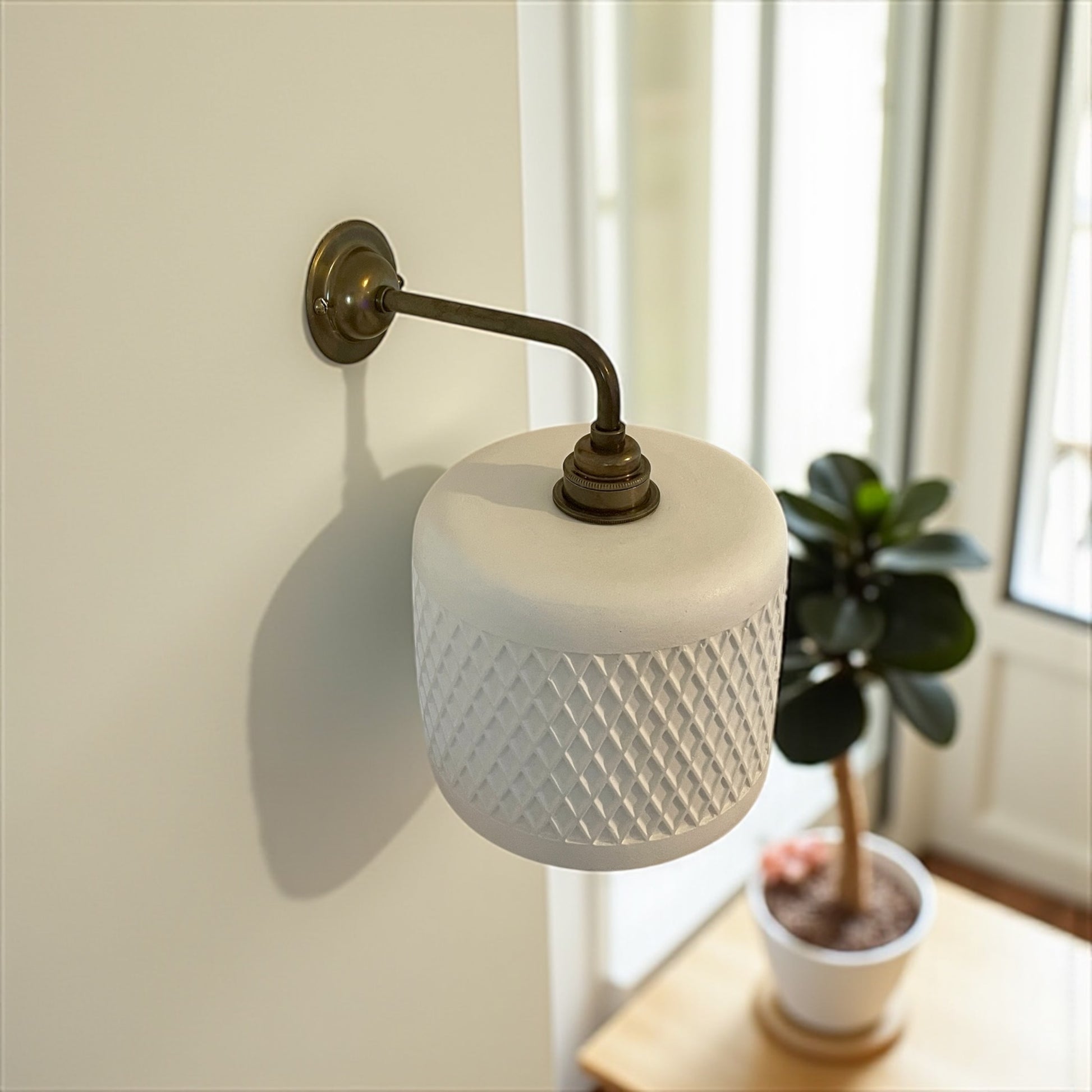 Wall-mounted sconce with textured white shade and brass arm in a room setting.