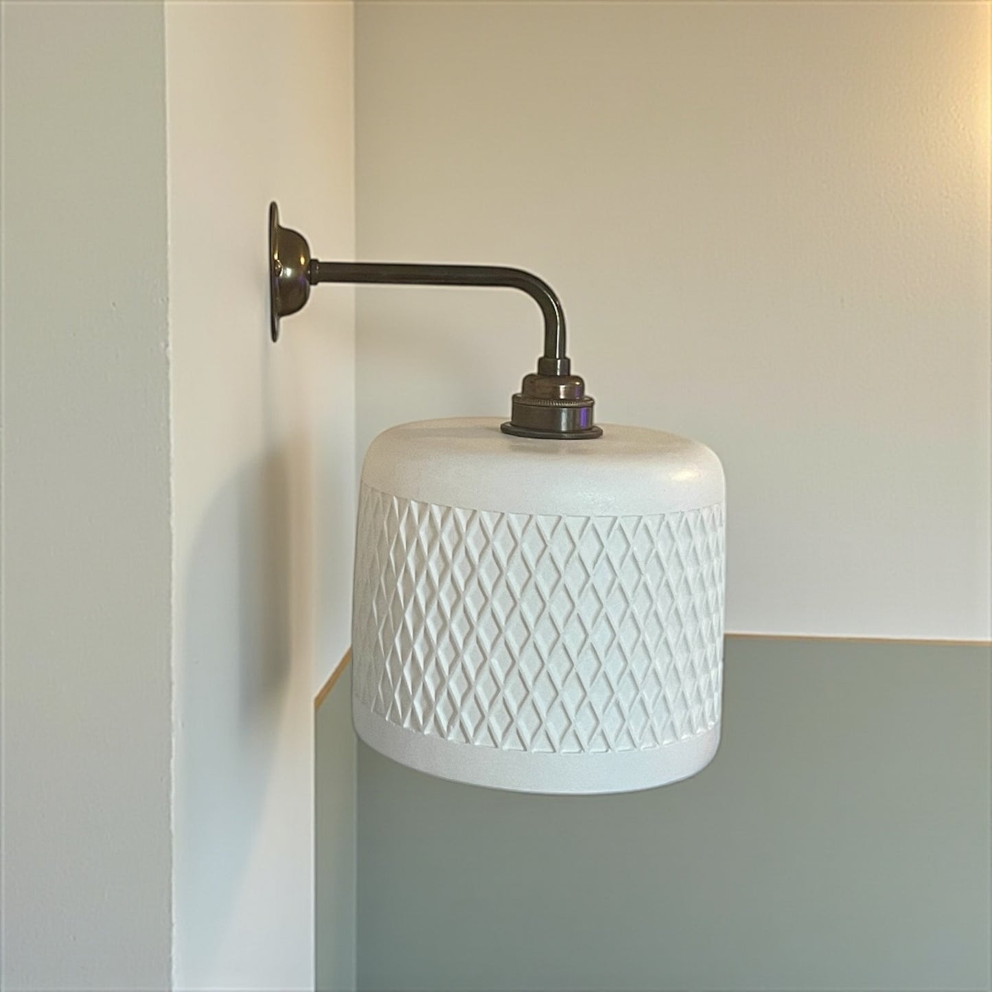 Wall-mounted lamp with white textured shade and metal arm against a neutral wall.