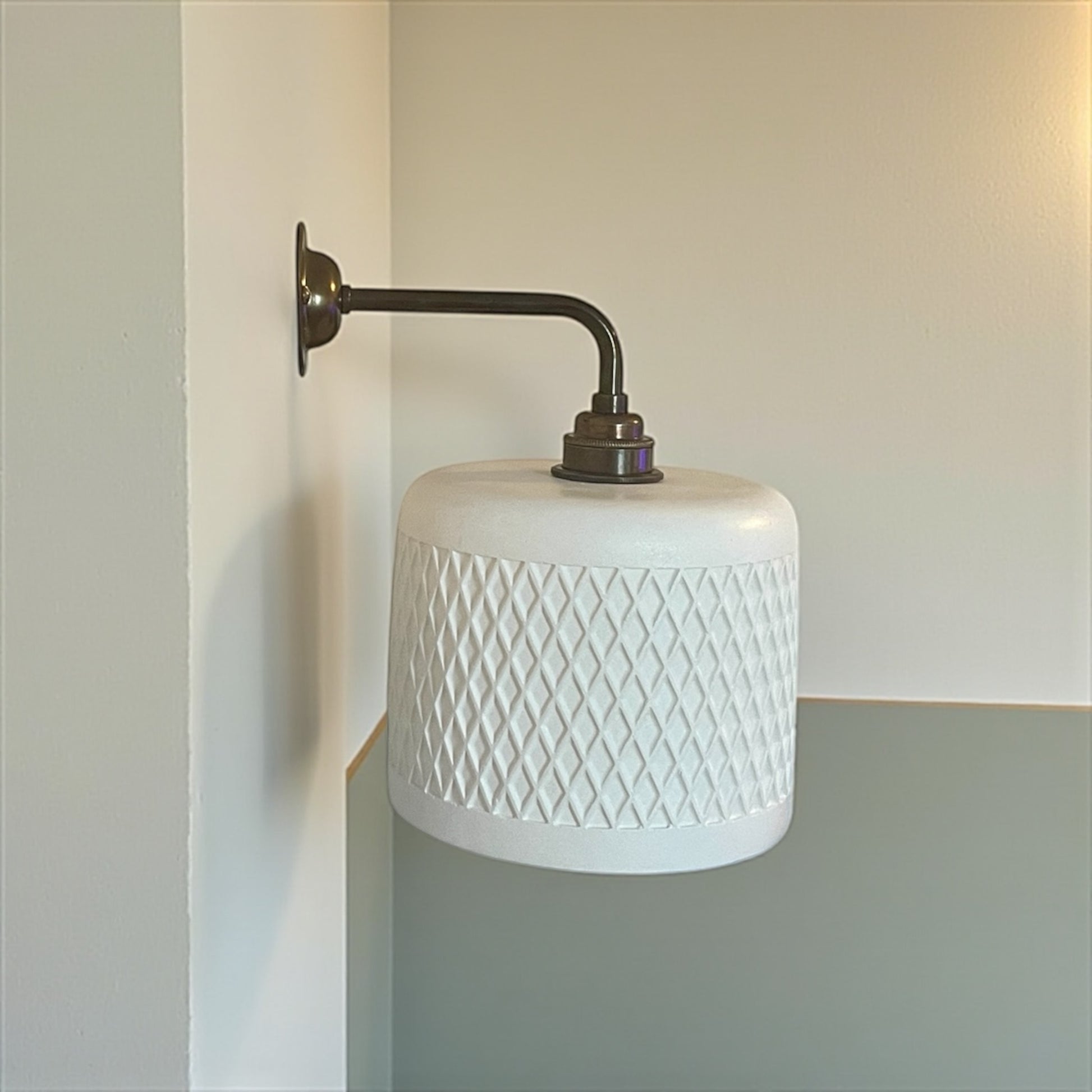 Wall-mounted lamp with white textured shade and metal arm against a neutral wall.