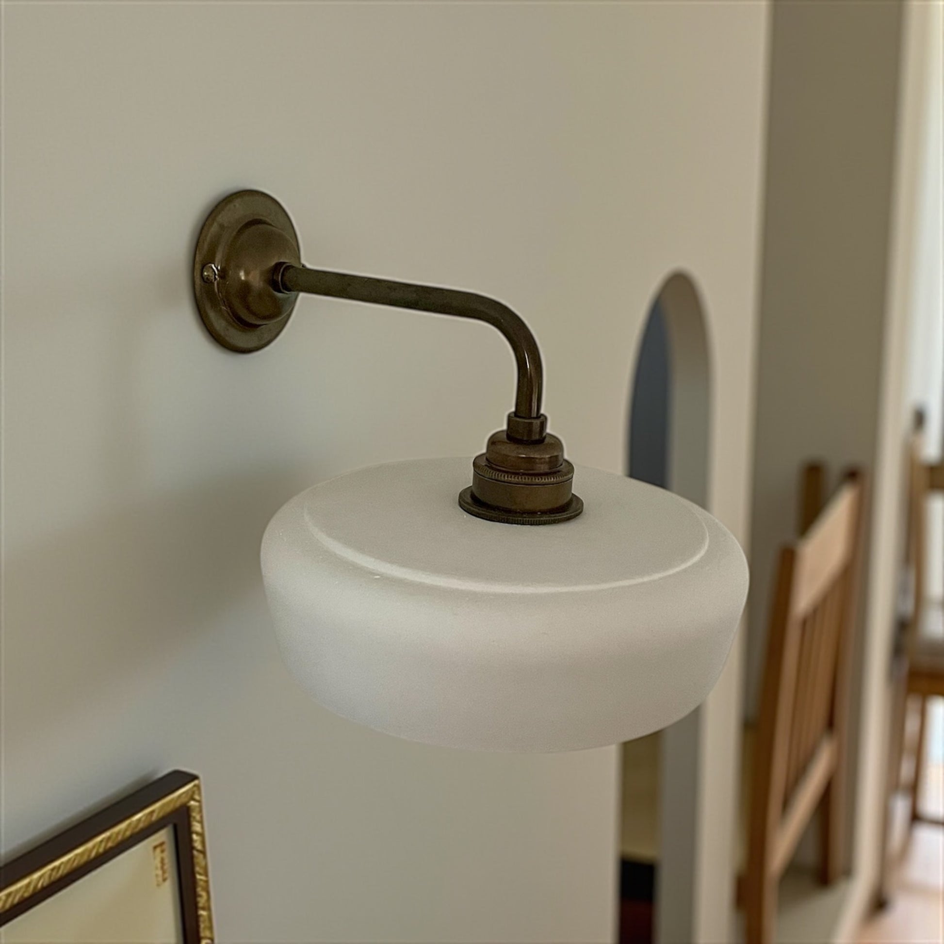 Wall sconce with white shade and brass arm in a room setting.