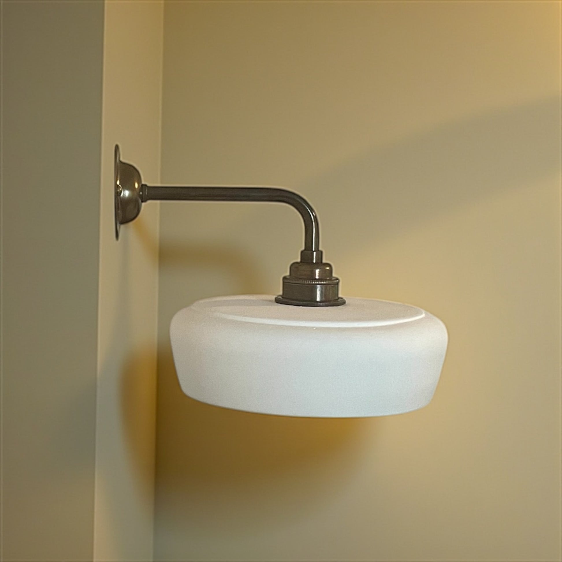 Wall-mounted light fixture with white glass shade and metal arm on a beige wall.