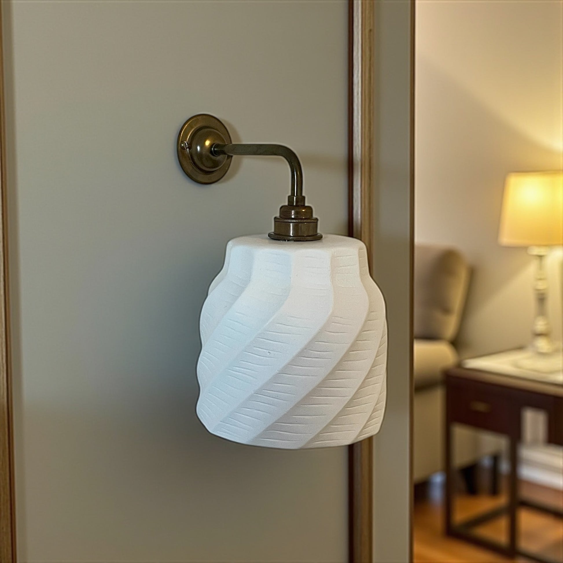 unique wall lighting fixture with textured white shade and brass arm in a room setting.