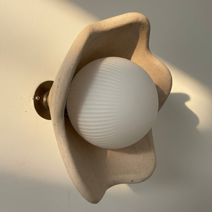 Wall-mounted light fixture with a beige shell-like design on a plain wall.