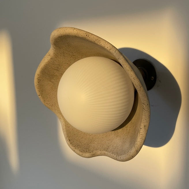 Wall sconce light fixture with a spherical bulb inside a decorative beige shell on a neutral background.