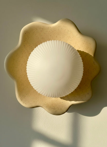 Sculptural wall light fixture with a textured beige base and white glass cover on a neutral background