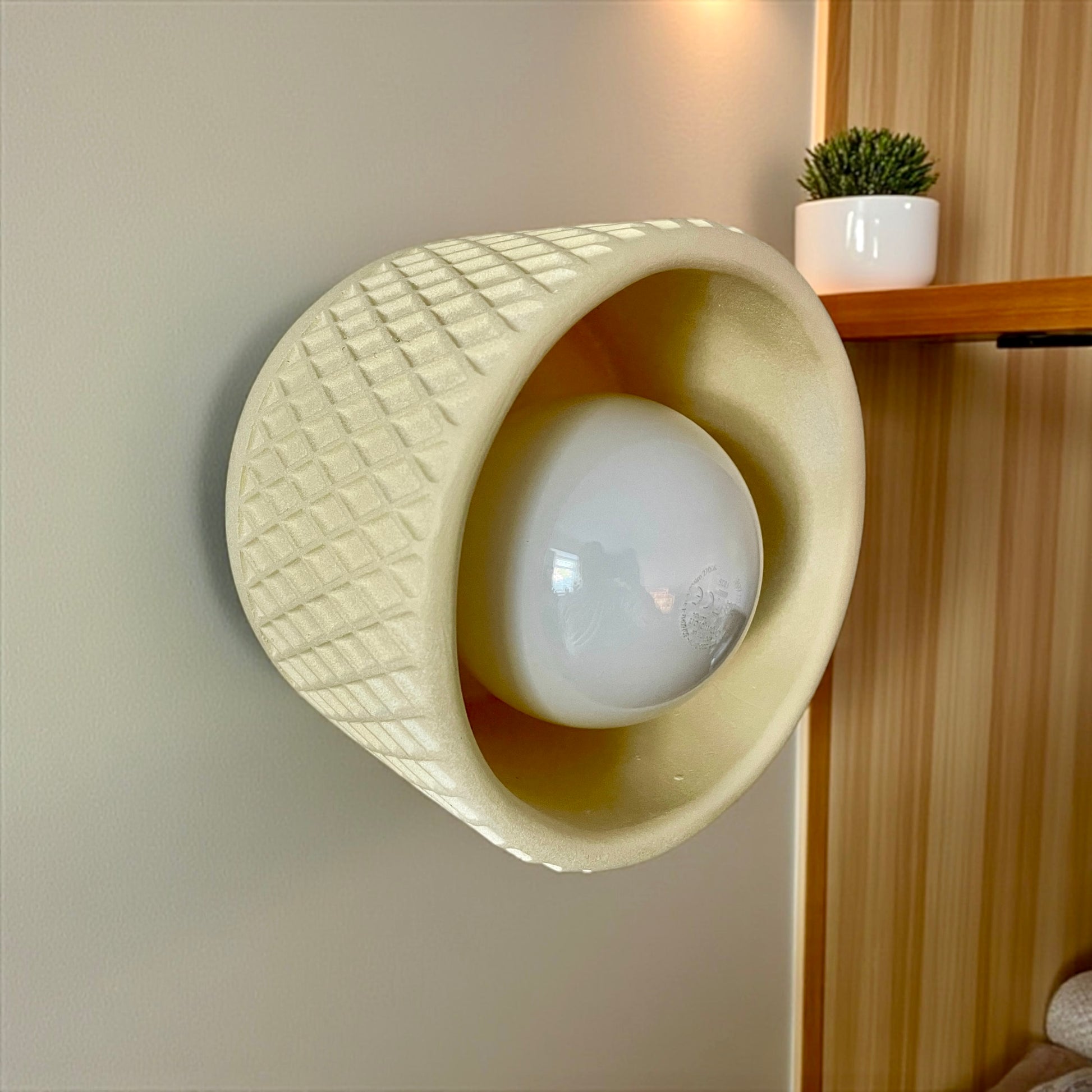 Ceramic wall light fixture with textured design on a neutral wall.