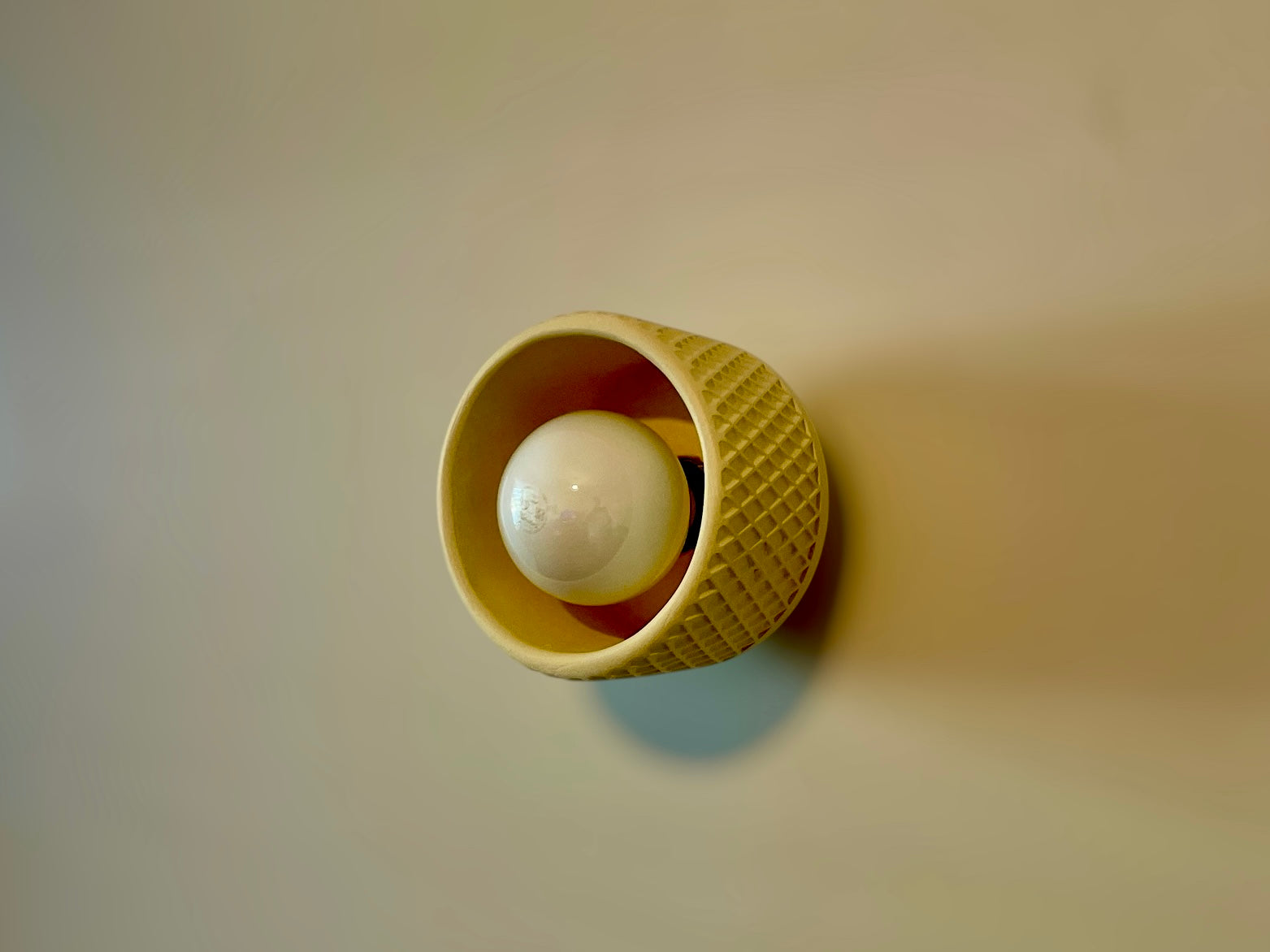 Ceiling light fixture with a textured beige cover on a beige wall.