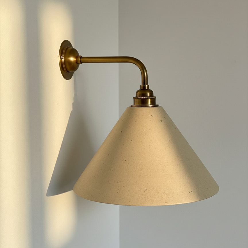 Beige wall light with beige cone shade and brass arm on a light gray wall.