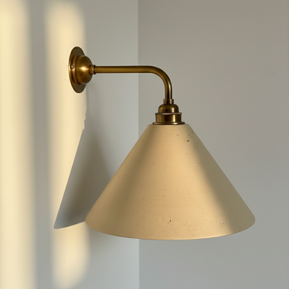 Beige wall light with beige cone shade and brass arm on a light gray wall.