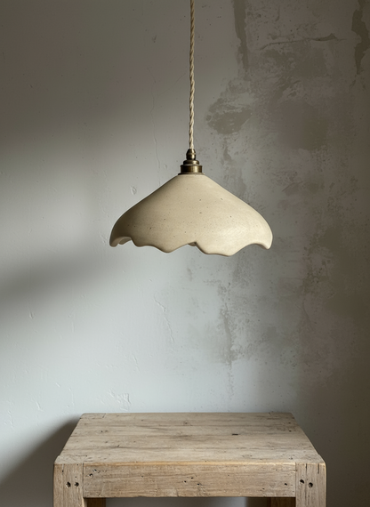 Beige handcrafted pendant lamp hanging above a wooden table against a textured wall.