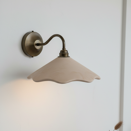 Wall-mounted lamp with a beige shade on a wooden surface next to a vase and mug.