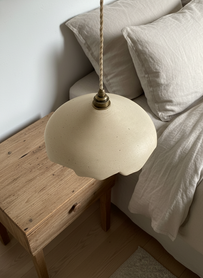 Beige pendant lamp hanging over a wooden side table with a bed in the background