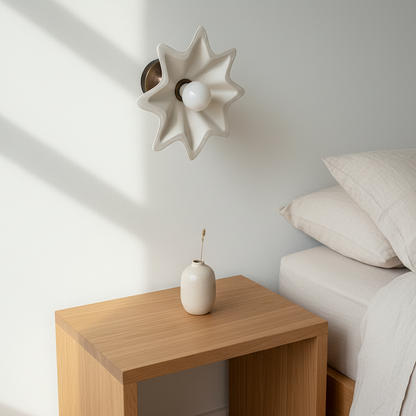 Neatly made bed with beige bedding and pillows in a room with a wooden nightstand and decorative wall light.