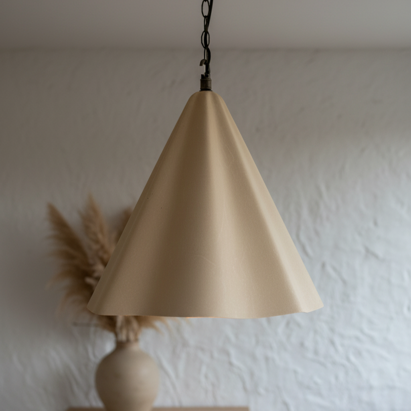 Beige cone-shaped pendant light hanging against a white wall with a vase and dried plants.