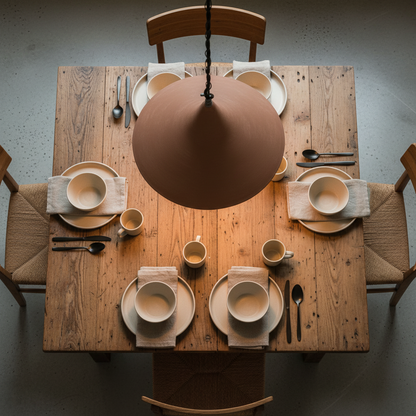 Dining table set with ceramic plates, cups, and cutlery under a brown pendant light.