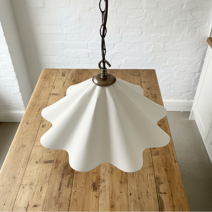 White scalloped pendant light on a wooden table with a white brick wall background