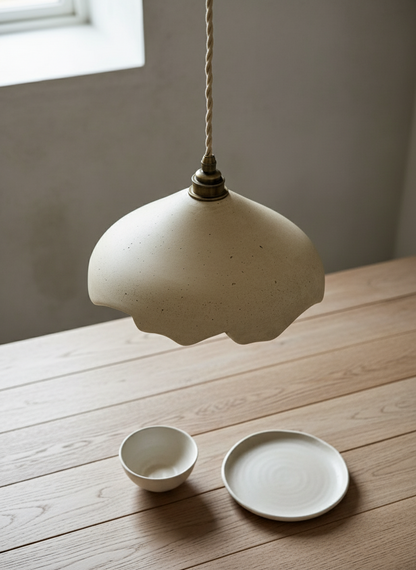 Handmade plaster pendant light hanging above two small ceramic dishes on a wooden surface.