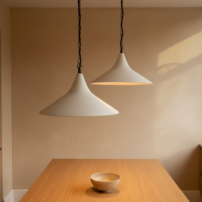 Two pendant lights hanging above a wooden table with a bowl on a beige wall background.
