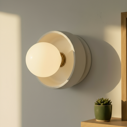 Flush mount wall light fixture with a soft glow on a neutral wall, next to a small potted plant.