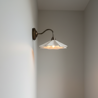 Wall-mounted lamp with a white shade on a plain wall, next to a wooden table with a ceramic bowl.