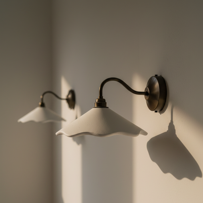 Two wall-mounted lights with white shades and black metal arms on a plain wall.
